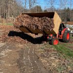 A full barrow of leaf mulch being put onto the ground from a tractor.