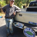 Richard Robinson leaning on a truck that has "Real Organic" sign attached to the back.